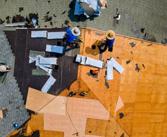 Aerial top view of construction roofer installing roof tiles at house building site at work installing roof shingles