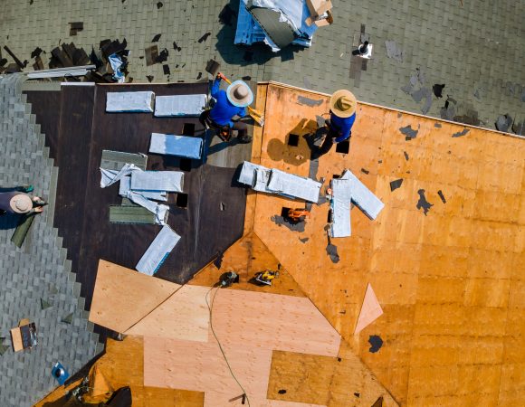 Aerial top view of construction roofer installing roof tiles at house building site at work installing roof shingles