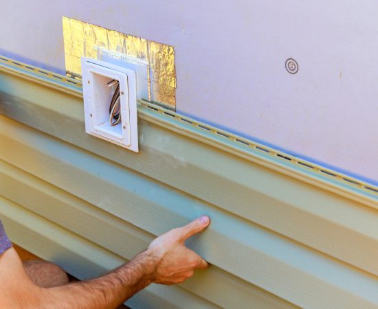 Vinyl plastic siding panels are installed on wall facade of new building by an employee